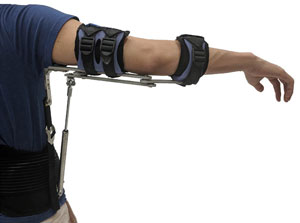 A man’s arm is being held straight out to his right by metal connected to straps on his arm and a waist band.