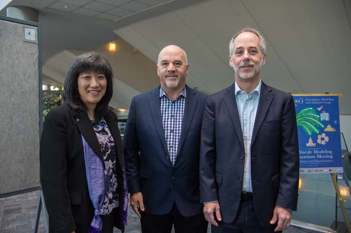 Organizers Grace Peng and Jeff Holmes welcome keynote speaker Charles Taylor, at center. three people in conference center