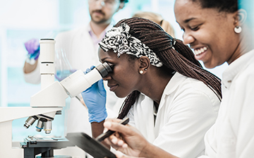 woman looking into microscope in lab