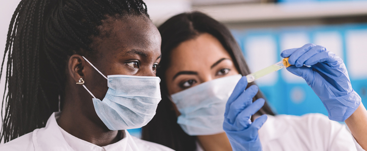 Two women wearing masks and looking at a vial