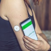 Mujer checando el nivel de glucosa con sensor y teléfono móvil