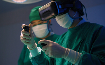 Photo of two doctors with masks with one doctor wearing a virtual reality headset and holding virtual reality remotes