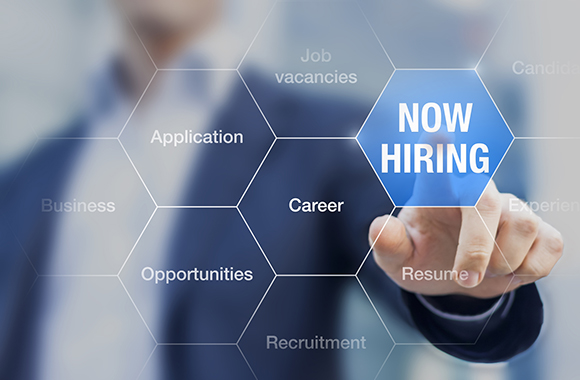 Now hiring sign in focus with person pointing from background