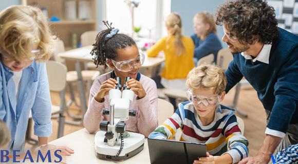Three children and a teacher with one child looking in a microscope and another looking at a tablet