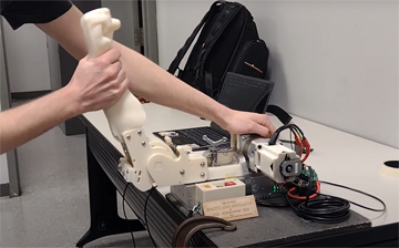 A student pulls on the wrist of the SpasTECH mechanical arm