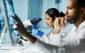 Photo of a man looking at a screen and a woman looking in a microscope