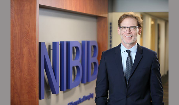 photo of Director standing next to sign that says NIBIB