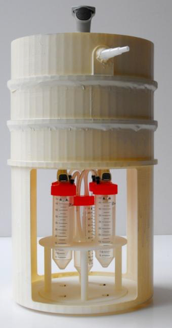 A photo of the microflora refinement system, a white bin with three tubes with red caps attached to the bottom spout.