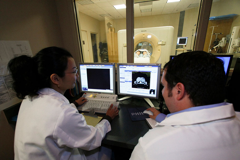 This is a picture of two radiologists viewing a CT scan on a computer as the scan is being conducted.