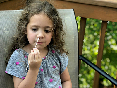 Girl uses a swab to extract a specimen sample for COVID-19 testing from her nostril