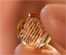 Image of a transparent hexagon with multiple dots on it being held between two fingertips Image of a transparent hexagon with multiple dots on it being held between two fingertips
