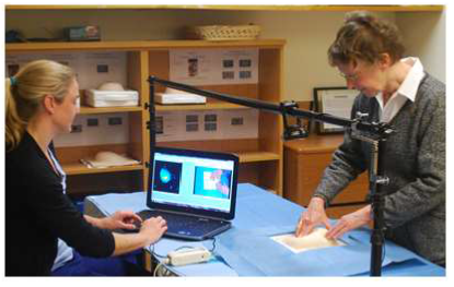 Physician practicing breast exam on model as technician records breast exam technique on computer