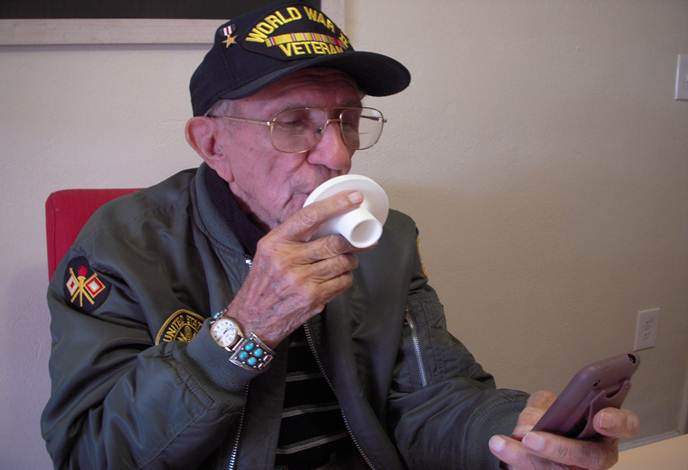 A photo of an elderly man bringing a small, circular, plastic device to his mouth.
